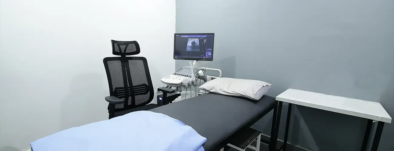 A cardiac imaging room with a bed, chair, and monitor.